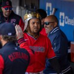 Baseball player in a red Indians jersey wearing a gold crown helmet in the dugout, high-fiving a teammate.