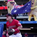 Guardians player in a red uniform in the dugout, with inflatable mascots behind him holding an Australian flag.