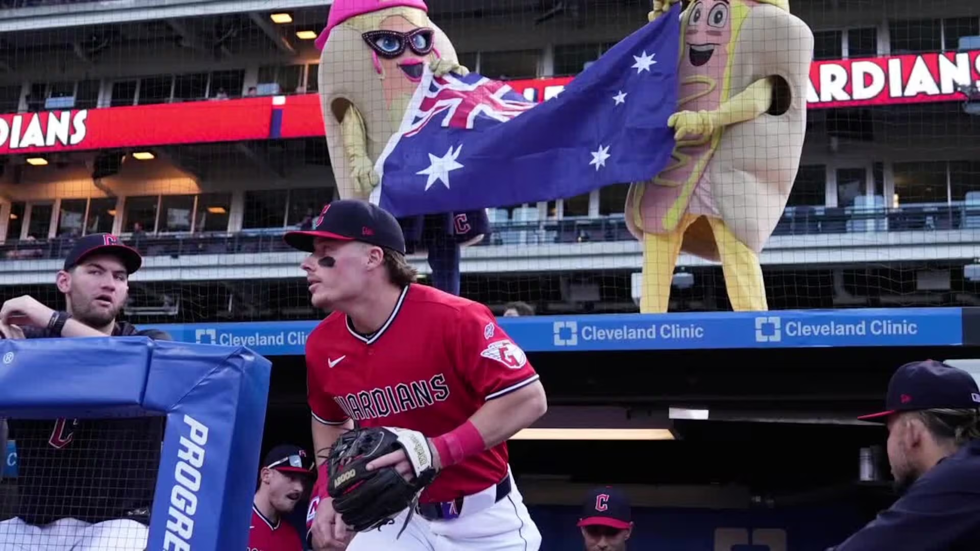 Guardians player in a red uniform in the dugout, with inflatable mascots behind him holding an Australian flag.