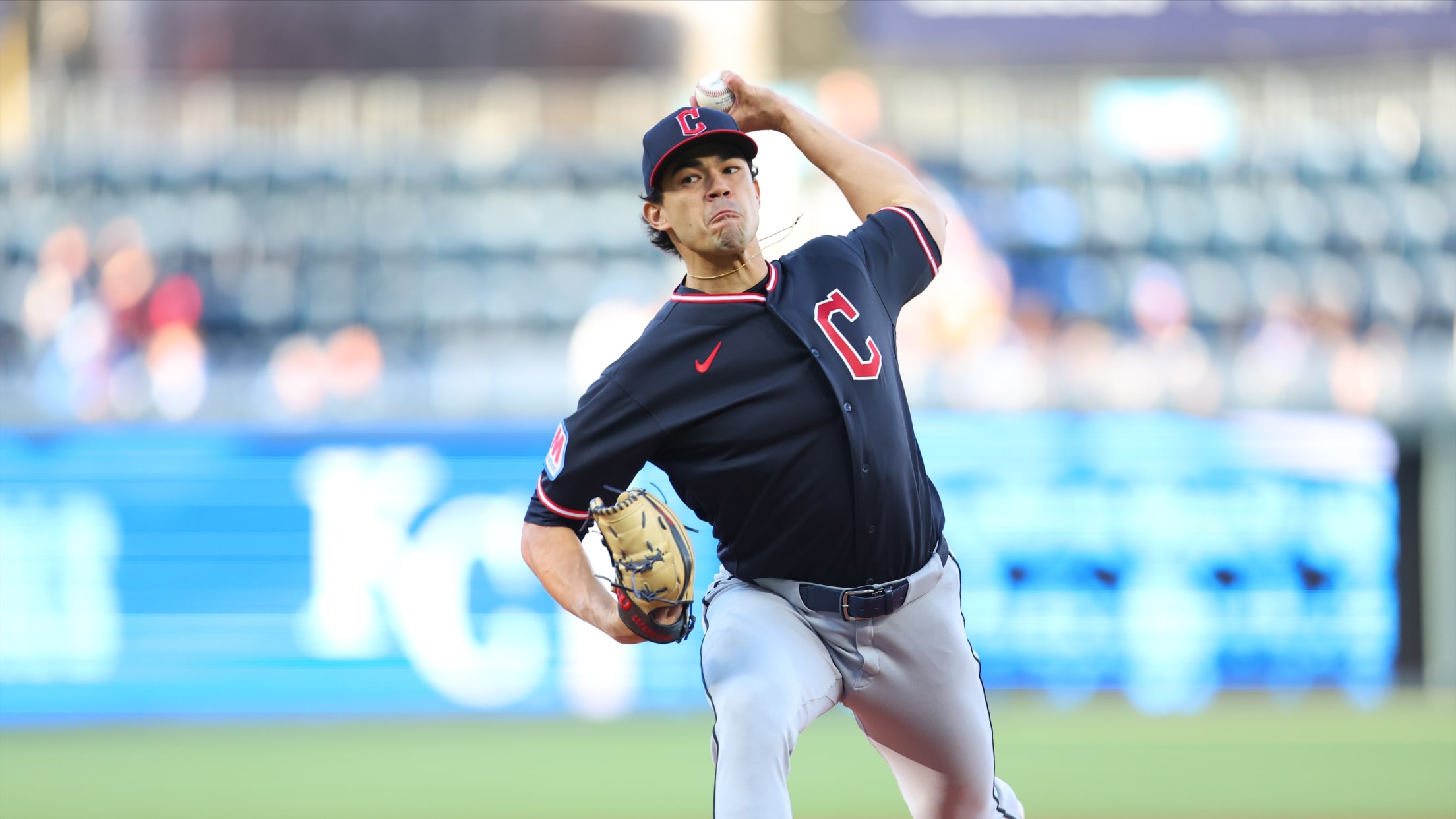 Baseball pitcher in a navy uniform mid-throw on the mound with a blurred stadium background