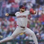 Cleveland pitcher in a gray uniform delivering a pitch on the mound with a crowd behind him.