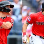 Two Guardians baseball players: left batter in red uniform with a black helmet swinging a bat; right runner in red jersey labeled 'Guardians'