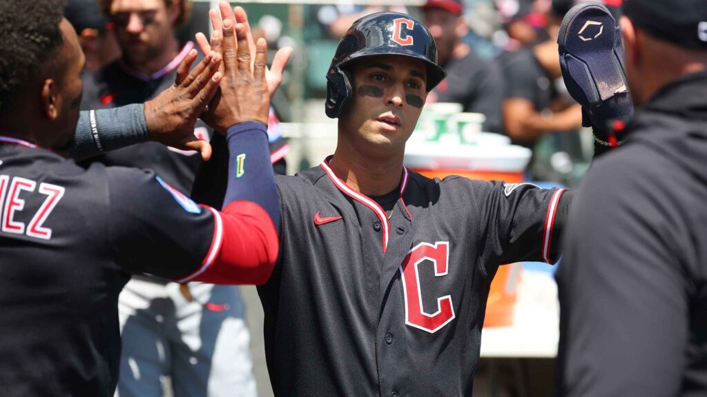 Baseball players in black uniforms give a high-five in a dugout area, celebrating the moment.