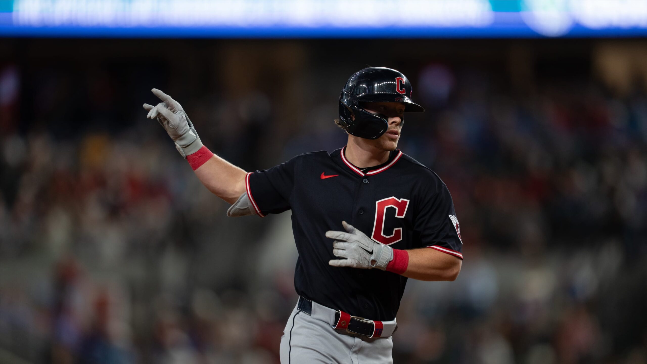 Baseball player in a black jersey with red trim and helmet, raising his right arm in celebration on the field.