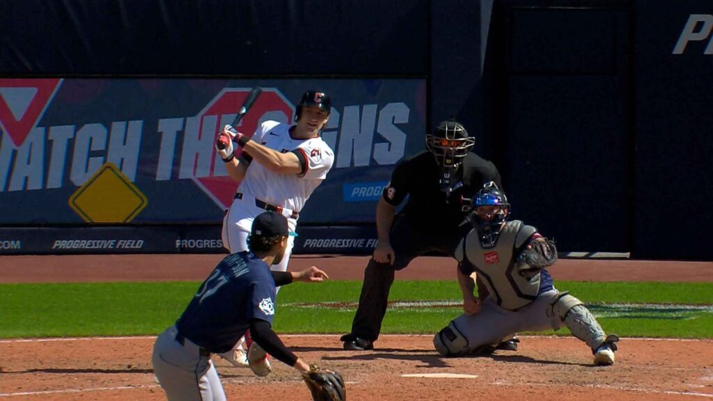 Baseball batter in white uniform swings at a pitch at home plate as catcher and umpire watch in the background.
